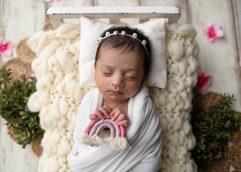 newborn baby posed on bed, baby holding rainbow, newborn baby rainbow photoshoot